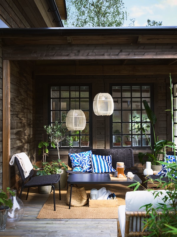 A cozy terrace with black TEGELÖN lounge furniture, blue and white pillows, and decorative SOLVINDEN lighting.